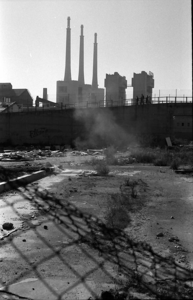 Vista llunyana de les tres xemeneies, amb un solar abandonat en primer terme. Foto en Blanc i negre