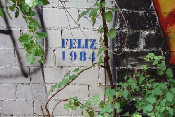 Paret amb un graffiti stencil que posa Feliz 1984