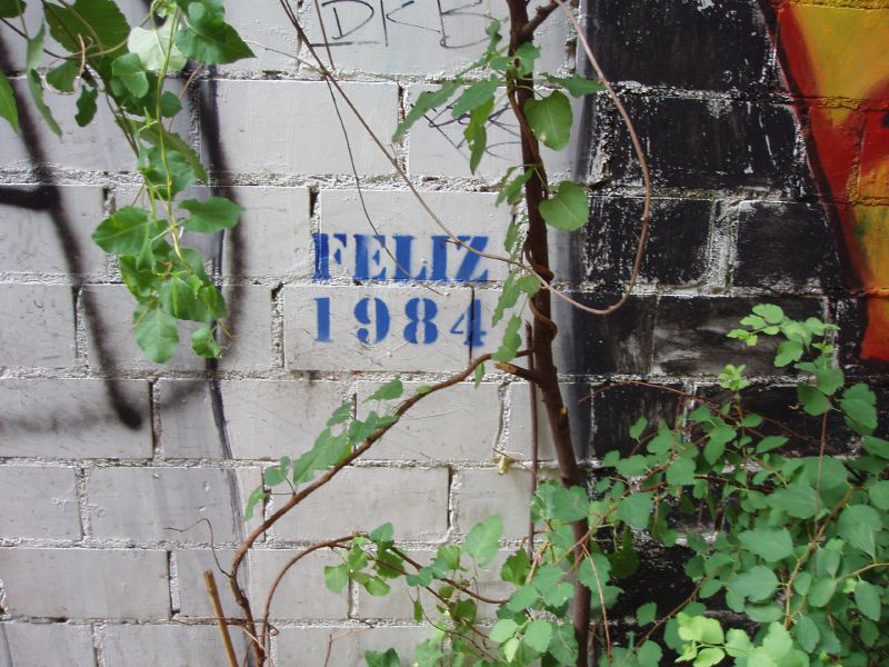 Paret amb un graffiti stencil que posa Feliz 1984