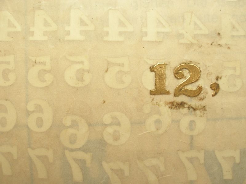 Full de letrayon amb un 12 daurat, es transparenten números que hi ha a l'altra cara