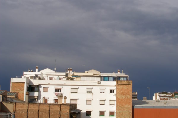 Vista del cel gris, fosc i amenaçant, però amb l'edifici amb la façana il·luminada pel sol