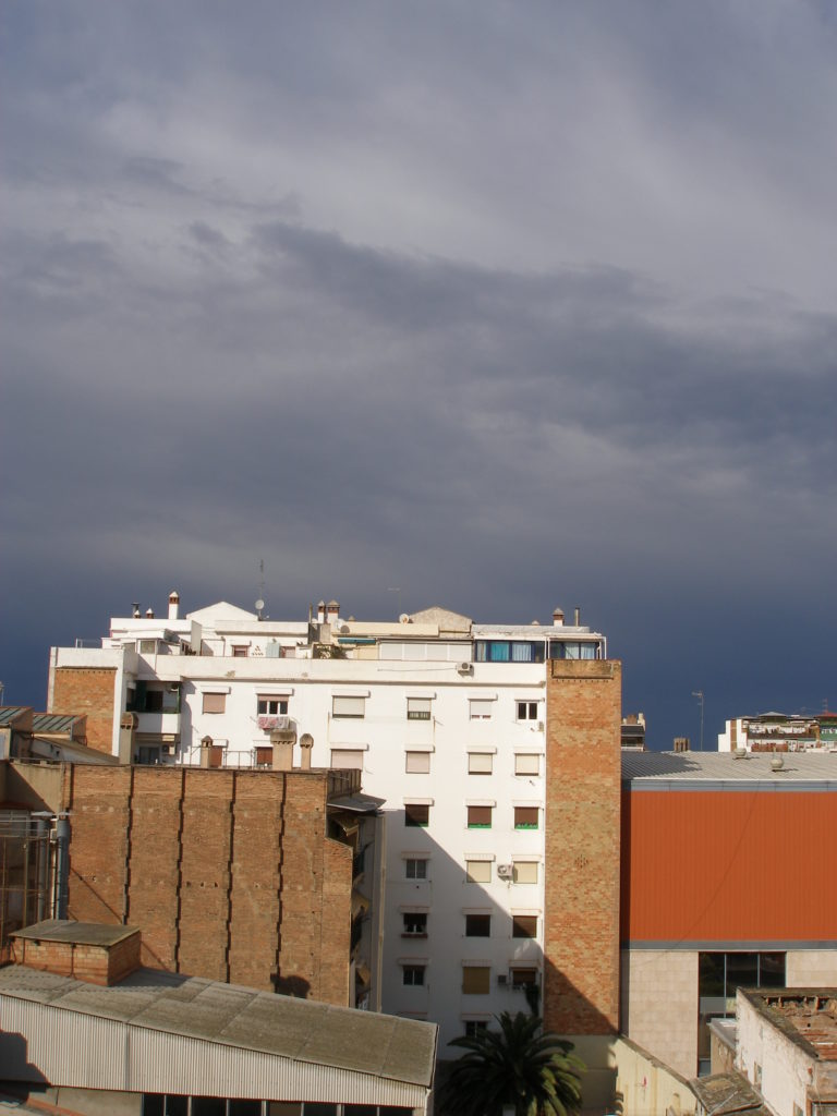 Vista del cel gris, fosc i amenaçant, però amb l'edifici amb la façana il·luminada pel sol