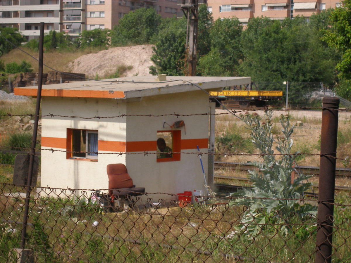 Des del tren, caseta molt precària de vigilància al costat de la via, es veu un home per la finestra