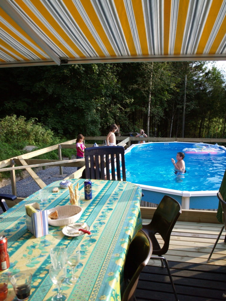 Nens banyant-se a la piscina, en primer terme la taula amb les restes del dinar i el toldo