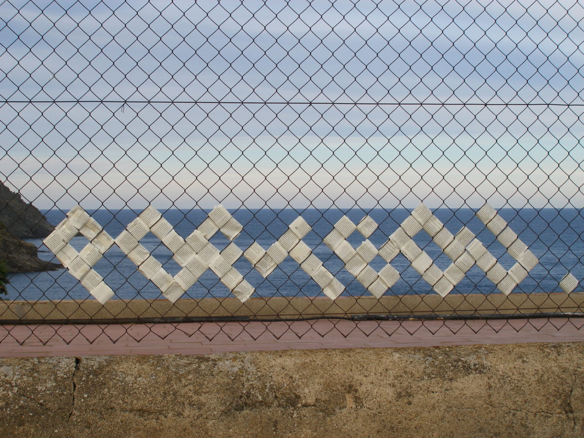 Composició de la paraula "portbou" en paper sobre una reixa amb el mar de fons