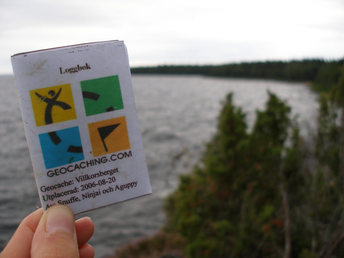 Llibreteta del Logbook del Geocaching amb el llac desenfocat de fons