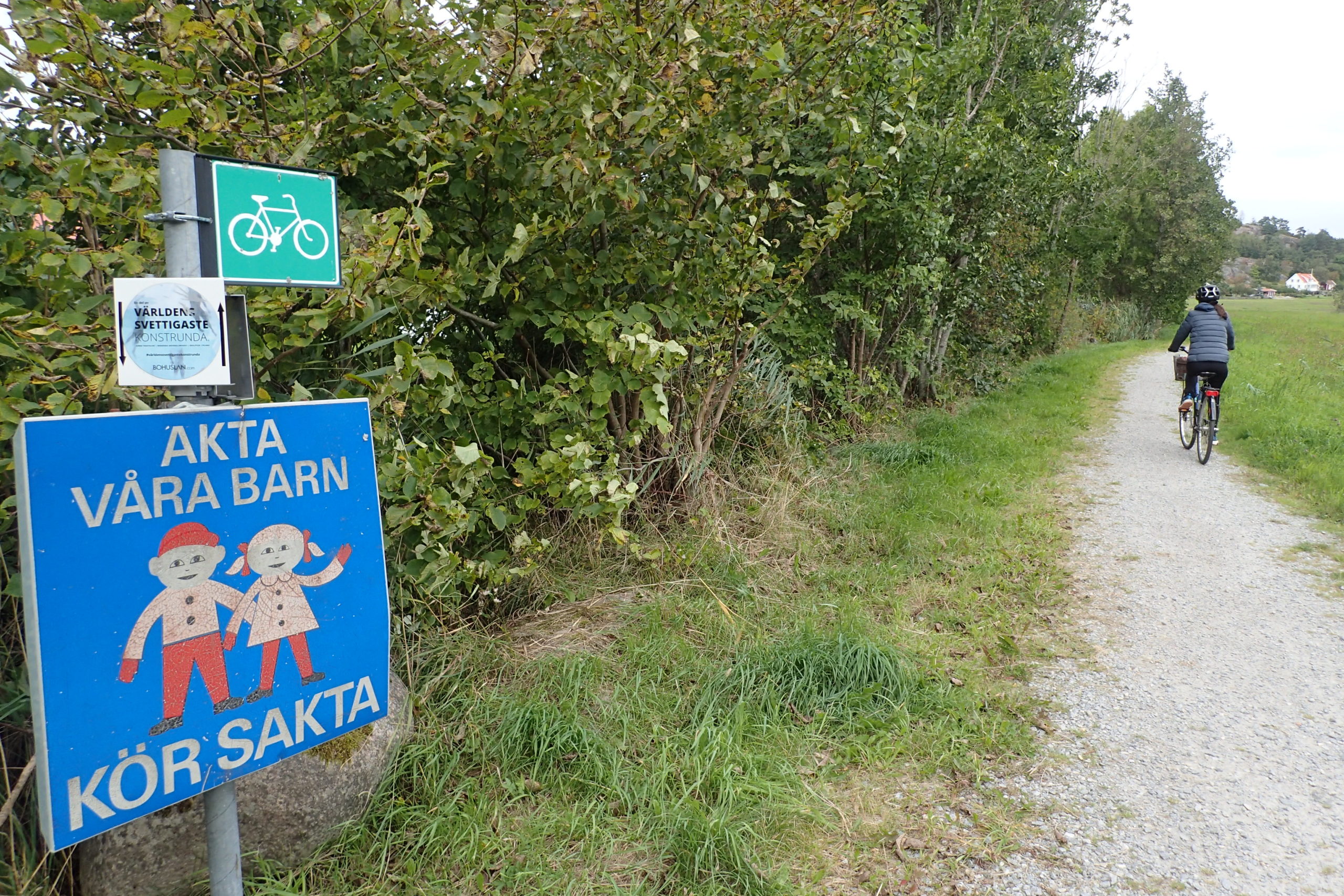 Amb la bici per un camí de grava. Rètol indicant la ruta de la bici. Senyal: compte amb els nostres nens, condueix poc a poc