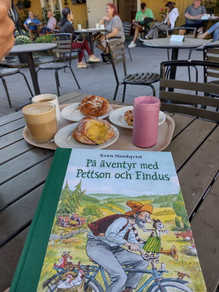 Fika en una terrassa, en primer terme el llibre "På aventyr med Pettson och Findus", de Sven Nordqvist