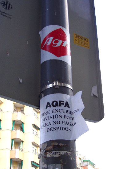 Pal d'un fanal amb una enganxina amb el logo d'Agfa i un paper a sota on s'hi llegeix: AGFA cierre encubierto división foto para no pagar despidos